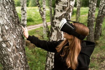 Fototapeta premium girl in virtual glasses touches a tree with a surprised face