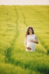 young pregnant woman in fieid of green grass. Young beautiful pregnant girl with a wreath on her head in the sun. Motherhood. Spring. copy space. selective focus