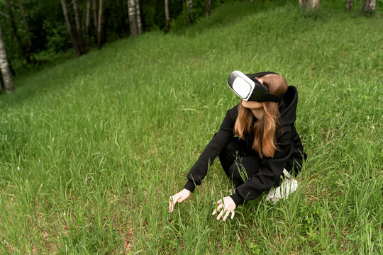 girl in virtual reality glasses touches the grass raising her head to the top