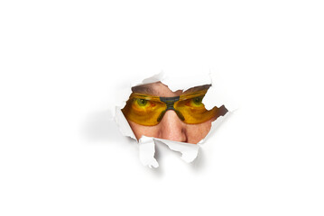 Man in shooting glasses peeping through hole on paper. Male in ellow glasses looking through hole....