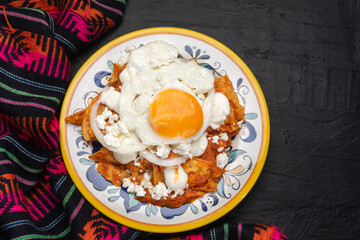 Mexican red chilaquiles with fried egg on dark background
