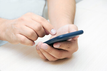 Fototapeta premium A person is holding a phone and tapping the screen on a white background with copy space. Concept of lifestyle business and mobile Internet technologies in the office