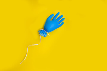 Quarantine Completion Concept. a blue medical glove flies like a balloon. on a bright yellow background.