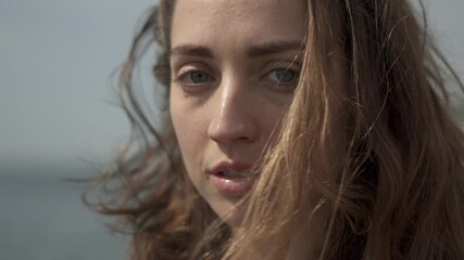 Young woman looking at camera while standing at seaside during sunny day