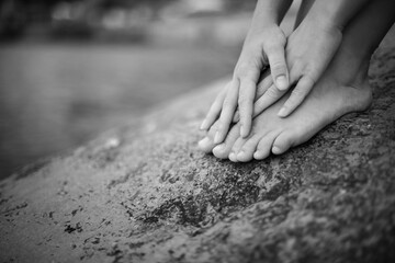 A girl sits on a stone, a rock by the sea, a fragment of arms and legs, black and white image.