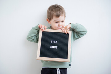 Toddler boy holding a felt letter-boad written Stay home. Stay home because of quarantine and self isolation. Social distancing. 