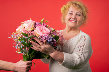 Naklejka premium hands of a young woman giving a bouquet of tulips to an elderly woman.march 8, mother's day concept