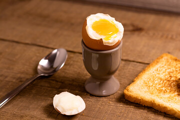 Opened boiled egg in an egg cup with yolk with a slice of toasted toast bread and a spoon on a...