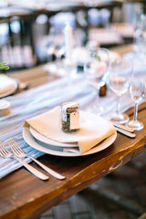 Vertical frame. Close-up seating spot the wedding guest with a set of dishes, napkin, glasses and a gift on a rustic wooden table. Modern outdoor wedding decorationconcept