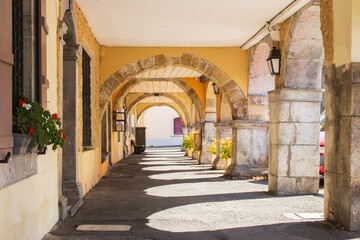 Medieval arches with flowers and lantern. Empty archway in France. Yellow arcade on sunny day. Ancient european architecture. Corridor with arches in old village building horizontal. Travel concept. 
