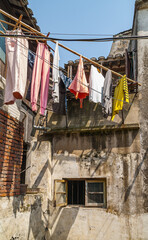 Tongli, JIangsu, China - May 3, 2010: Closeup of colorful laundry hanging off bamboo pole in courtyard of dilapidated hutong house under blue sky.