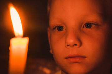 Concept of tragedy and loss. Child looks with sad eyes at burning candle in dark. Fire symbolizing memory of dead. Loneliness and religious sacrament. Lonely believing kid pray with hope in church