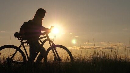 Fototapeta na wymiar free girl travels with bicycle in sunset. Healthy young woman tourist goes with bicycle along hillside, enjoying nature and fresh air. adventure and travel concept. women cyclist overcomes an obstacle