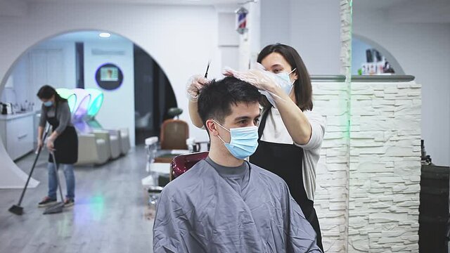 Man client in mask during hair cut by professional hairdresser in mask at beauty salon 