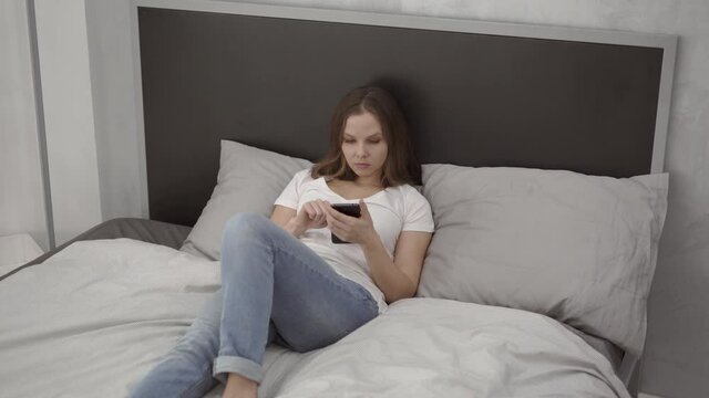 Woman lying on bed using smartphone at home