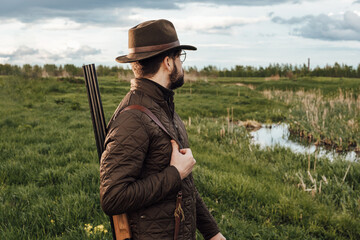 Naklejka na ściany i meble Vintage hunter walks. Rifle Hunter Silhouetted in Beautiful Sunset or Sunrise. Hunter aiming rifle in swamp and field