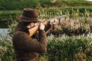 Fototapeta premium Vintage hunter walks. Rifle Hunter Silhouetted in Beautiful Sunset or Sunrise. Hunter aiming rifle in swamp and field