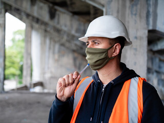 A construction worker in a construction helmet and protective antiviral mask puts a ballpoint pen...
