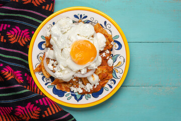 Mexican red chilaquiles with fried egg on turquoise background
