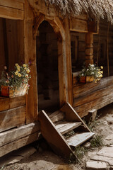 Fototapeta na wymiar Wooden antique porch, old thatched roof, violet flowers on the porch