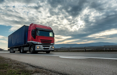  Red transportation semi trailer truck on a highway driving at bright sunny sunset. 

Transportation vehicle