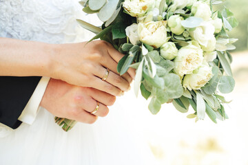 Obraz na płótnie Canvas Closeup view of newlyweds hands holding colorful wedding bouquet. Bride and groom wearing wedding rings. Outdoor background. Wedding day concept.
