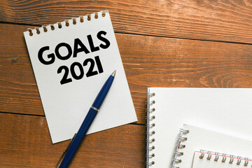 GOALS 2021 words written on a white piece of paper laid on a wooden table. Top view, concept in business.