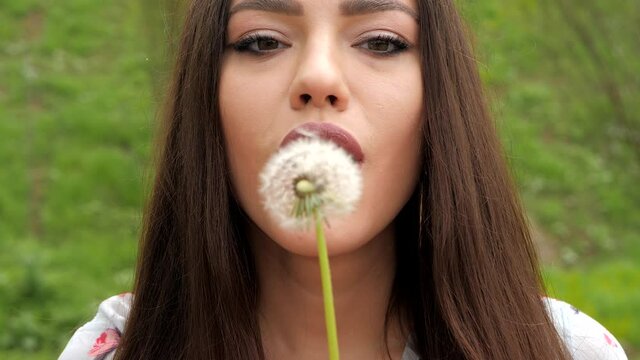 Close up view of attractive girl blowing off dandelion. Green background, summertime. 