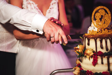 Obraz premium Wedding couple cutting wedding cake. Bride and groom holding knife in hands together. Marriage cooperation. Wedding day concept.