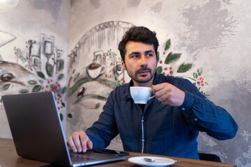 Brunette man working in cafe with computer and coffee