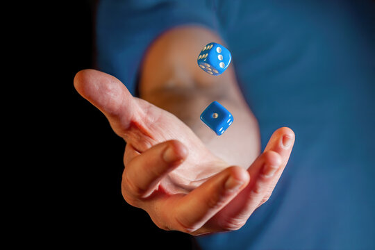 Caucasian male hand throwing blue dice cubes in the air - closeup with shallow focus
