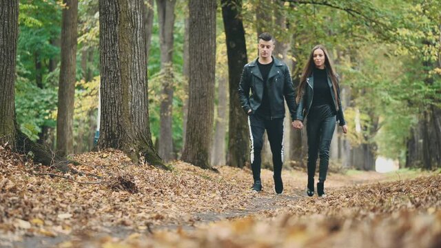 A loving couple walks in autumn park. Total black look. Blurred background. Crop. Copy space. 4K.