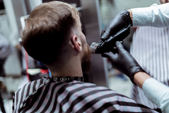 Foto detalle de maquina de barbero cortando barba a cliente en barber&iacute;a profesional