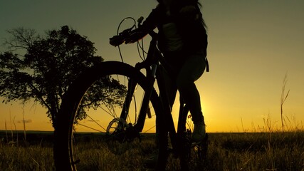 Fototapeta na wymiar Healthy young woman tourist rides bicycle in rays of an elephant, enjoying nature and fresh air. free girl travels with bicycle in sunset. Travel concept. woman cyclist overcomes an obstacle