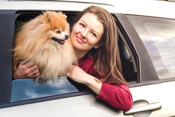 happy beautiful girl, woman, lady with pomeranian spitz dog in car travel. vacation concept with pet.