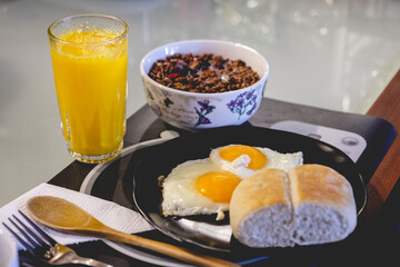 Breakfast with bowl with chocolate cereal and vegetal milk, fried eggs, bread and orange juice at home (and wood spoon)