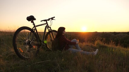 Fototapeta na wymiar single woman cyclist resting in park. free girl travels with bicycle in sunset. Healthy young woman hiker sitting on hill next to bicycle, enjoying nature and sun. concept of adventure and travel.