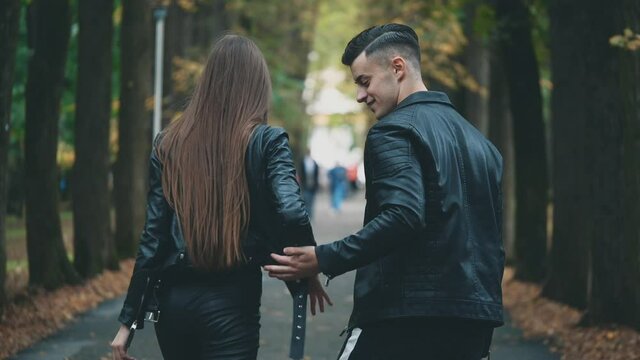 Boy in black leather coat and his lovely girlfriend met. They are walking along autumn park. Blurred background. Slow motion. Copy space. 4K.