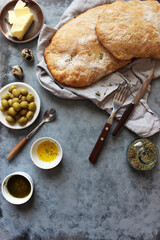 Ciabatta. Fresh italian ciabatta bread with herbs, olive oil and olives on grey background, top view, copy space.