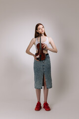 The girl in jeans and red sneakers plays the violin on a white background