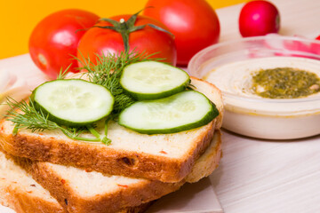 sliced cucumber on sliced bread, vegetables and a bowl with hummus in the background, vegan sandwich for breakfast, proper nutrition concept