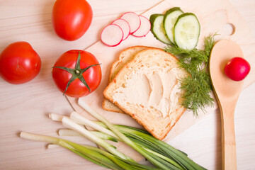 a piece of bread spread with hummus, vegetables and dill on a wooden table, ingredients for a vegan sandwich, healthy and tasty breakfast concept
