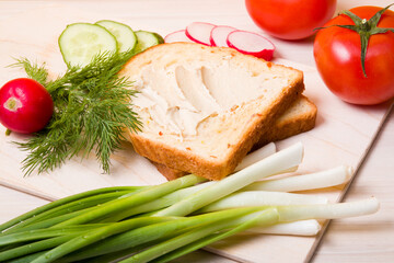 a piece of bread spread with hummus, vegetables and dill on a wooden table, ingredients for a vegan sandwich, healthy and tasty breakfast concept
