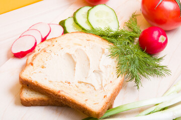 a piece of bread spread with hummus, vegetables and dill on a wooden table, ingredients for a vegan sandwich, healthy and tasty breakfast concept