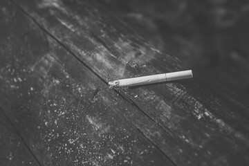 Black and white photo of a smoking and smoldering cigarette on a wood background
