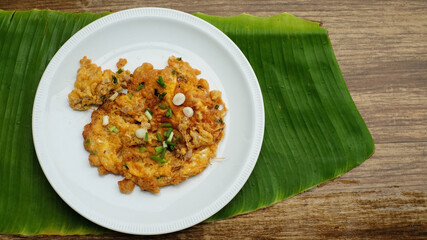 Fried eggs mixed pork chops with spring onion on top in white plate on banana leaf