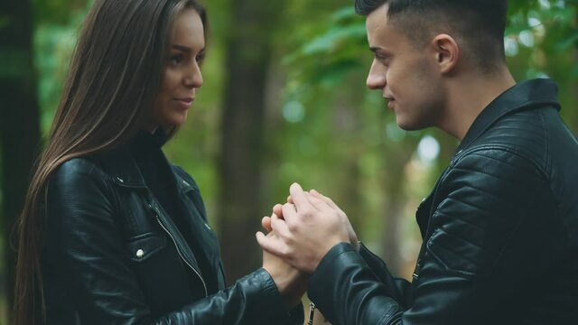 Couple is holding and warming up hands during cold autumn day. Handsome guy is kissing his girlfriend's hands. Close up. Blurred background. Crop. 4K.