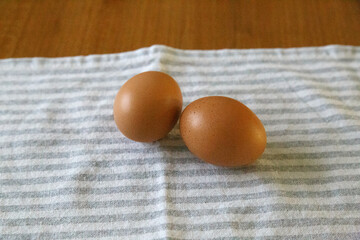 Front shot of 2 organic eggs on a white and gray dishtowel on a wooden table