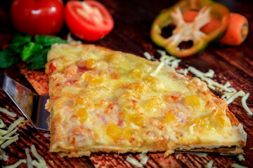 Front close-up of sweet Hawaiian pineapple pizza slice on dark wood background with fresh ingredients along