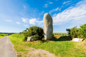 Large menhir stone in Ploguerneau, Brittany, France. A green meadow under the clear blue sky....